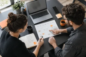 Overhead view of a small business owner and team member planning a social media content calendar at a charcoal desk with orange-accented stationery.